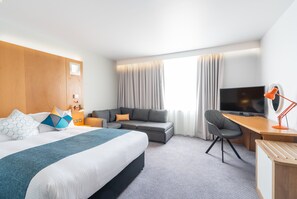 A hotel room with a bed, a sofa, a desk, a TV, and a lamp.