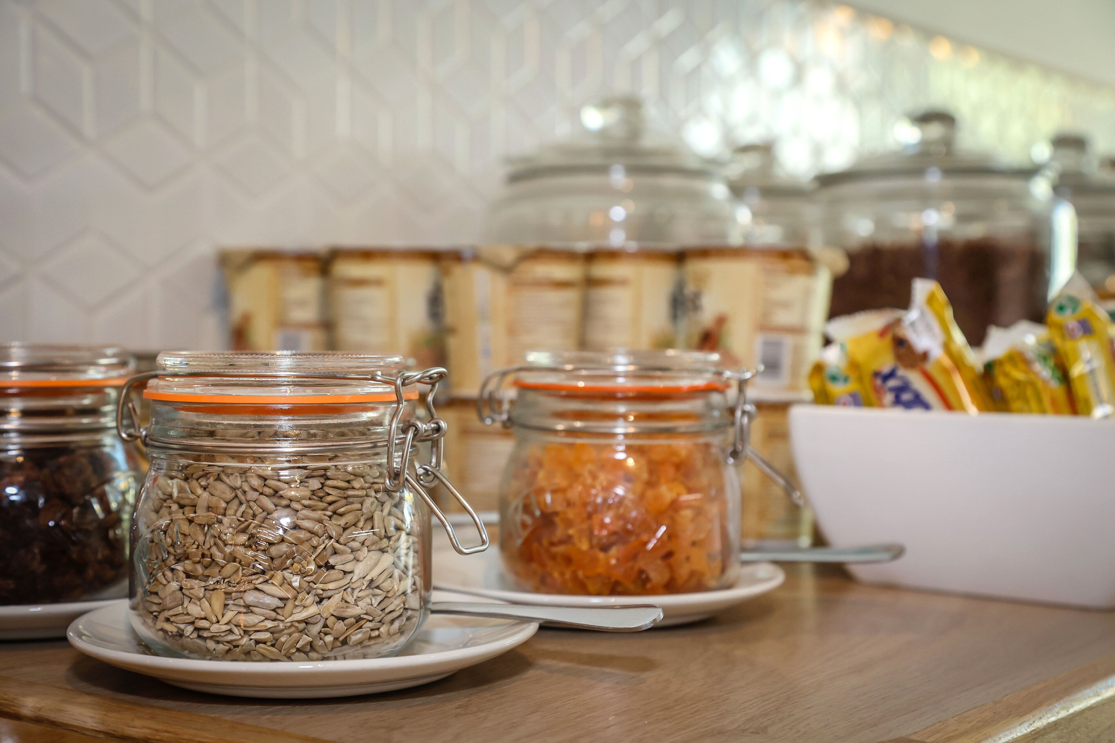 Ein Frühstücksbuffet mit verschiedenen Speisen in Gläsern und einer weißen Schüssel mit verpackten Lebensmitteln.