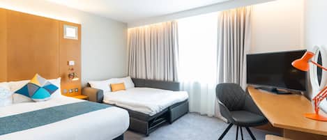 Habitación de hotel con cama, escritorio, silla, televisor y ventana con cortinas.