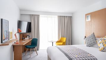A hotel room with a bed, a desk with a chair, a television, and a window with curtains.