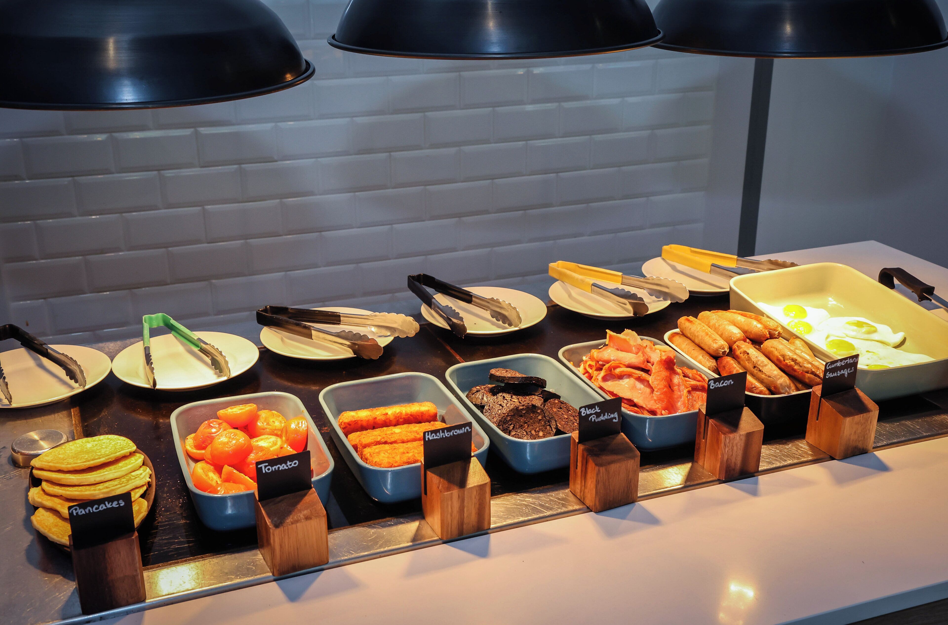 A buffet with various food options including pancakes, hashbrown, tomato, black pudding, and bacon.