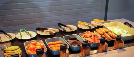 A buffet with various food options including pancakes, hashbrown, tomato, black pudding, and bacon.