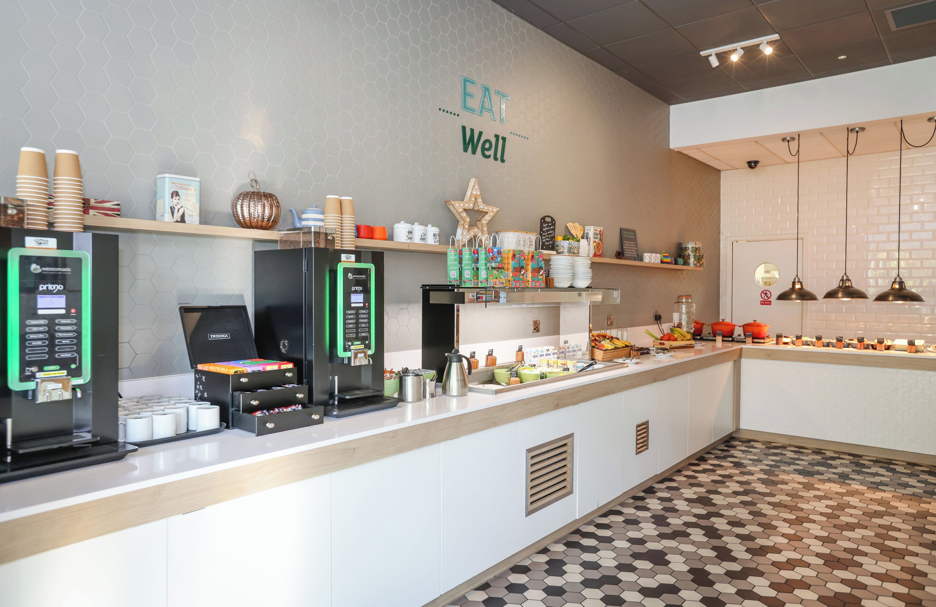 A modern cafe with a counter, coffee machines, and a variety of food items.