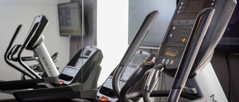 Equipo de ejercicio en un gimnasio con una pantalla digital, una pantalla en la pared y un ventanal.