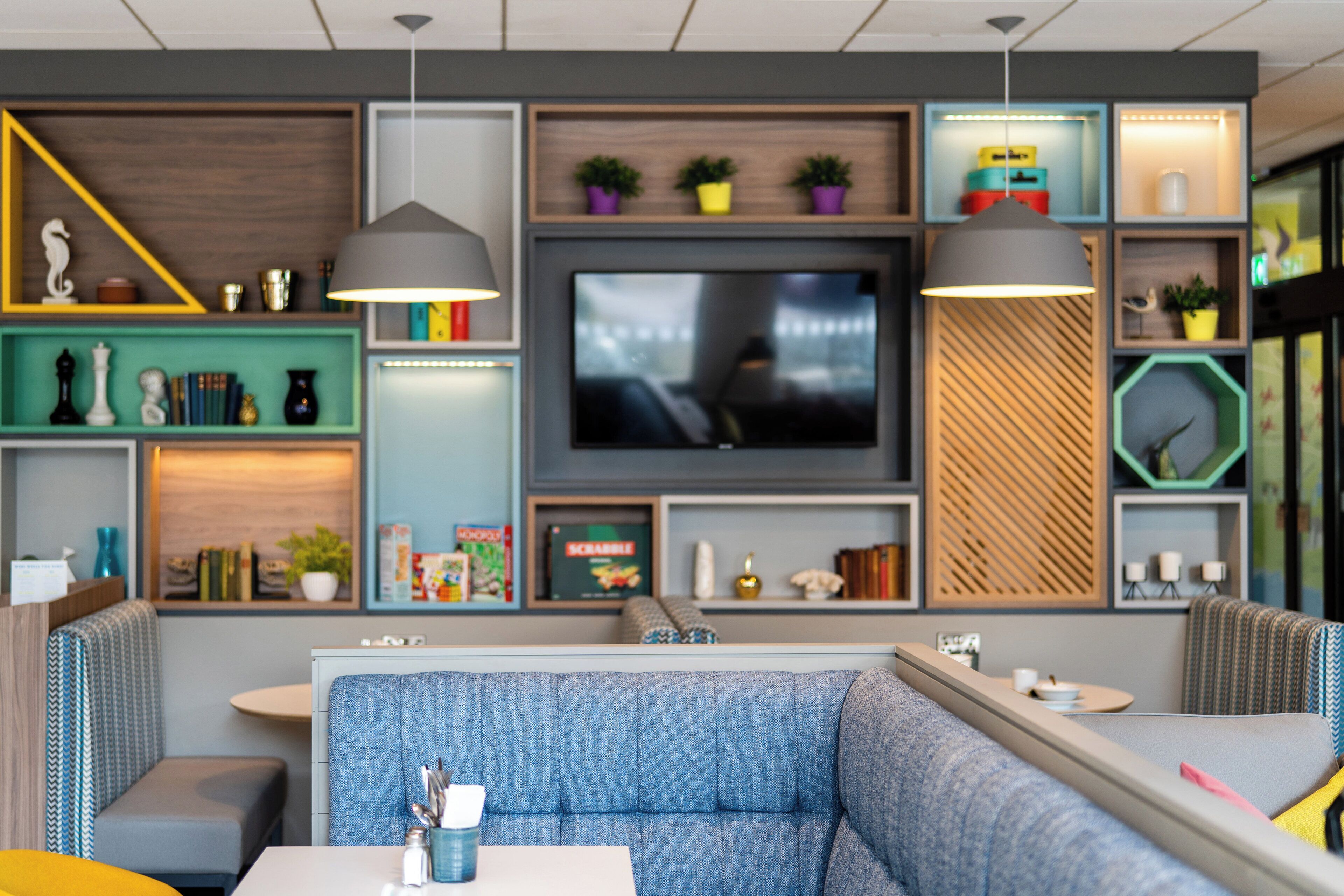 A modern living room with a sectional sofa, a flat-screen TV, and various decorative items on shelves.