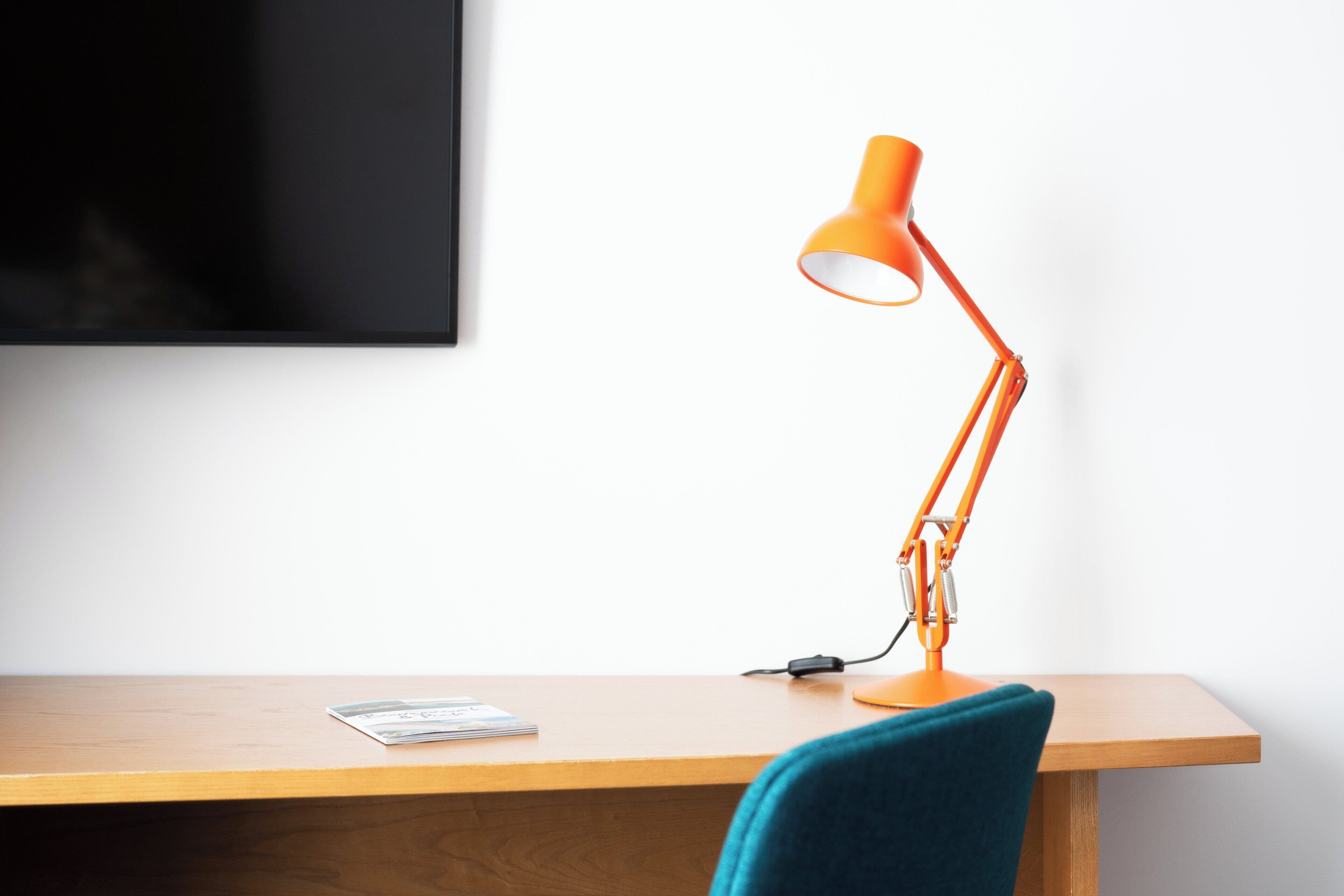 Ein Schreibtisch mit einer einzelnen orangefarbenen Schreibtischlampe, einem Stromkabel und einer Zeitschrift.