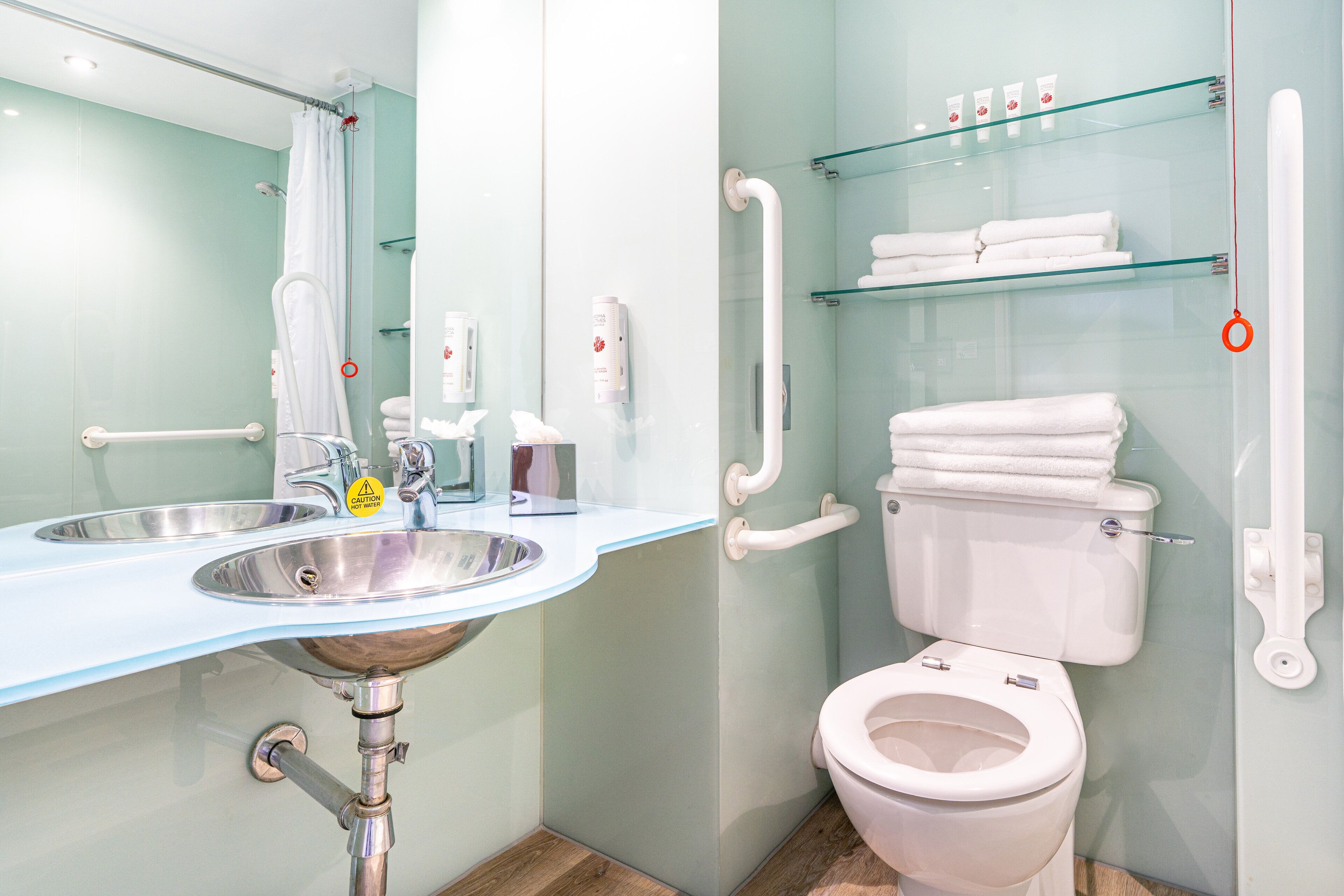Un baño moderno con un lavabo de vidrio, un inodoro blanco y un estante de vidrio con artículos de aseo.