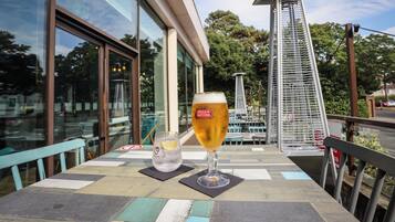 A table with a glass of beer and a glass of water, a chair, and a view of a building with large windows and a metal structure.