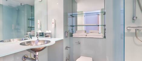 A modern bathroom with a glass sink, a toilet, and a shower area.
