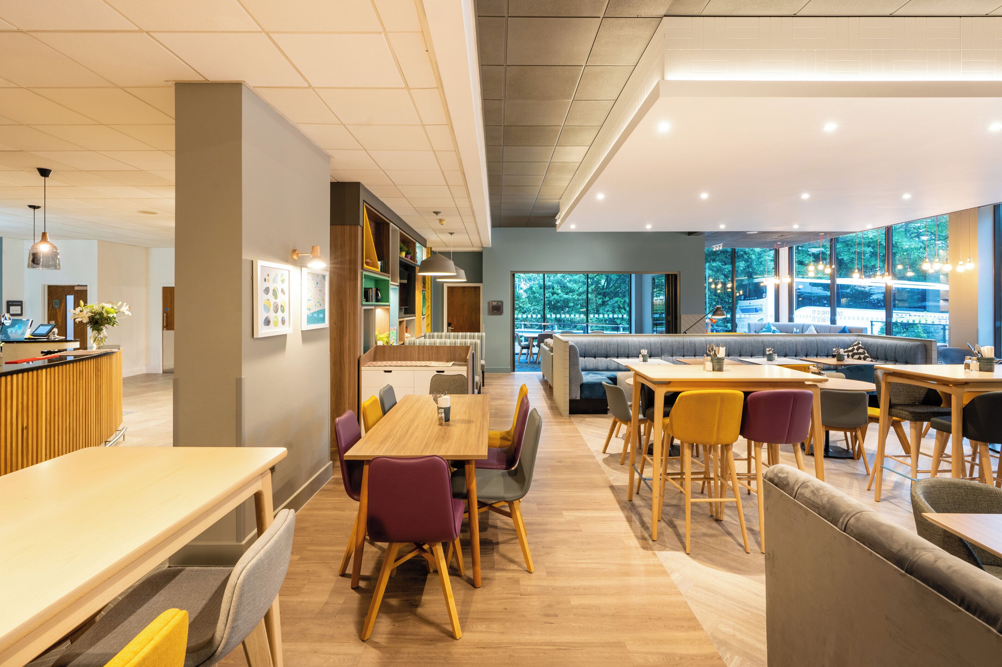 Un restaurante moderno con mesas y sillas de madera, una zona de bar y ventanas amplias con vistas al exterior.