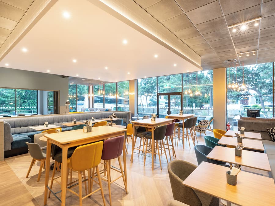 A modern cafe with seating arrangements, large windows, and a view of the outdoors.