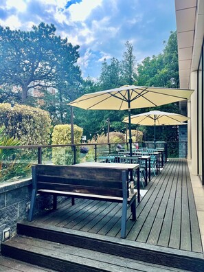 A wooden deck with outdoor seating, including tables and benches, under large umbrellas. - Holiday Inn Bournemouth by IHG (Bournemouth)