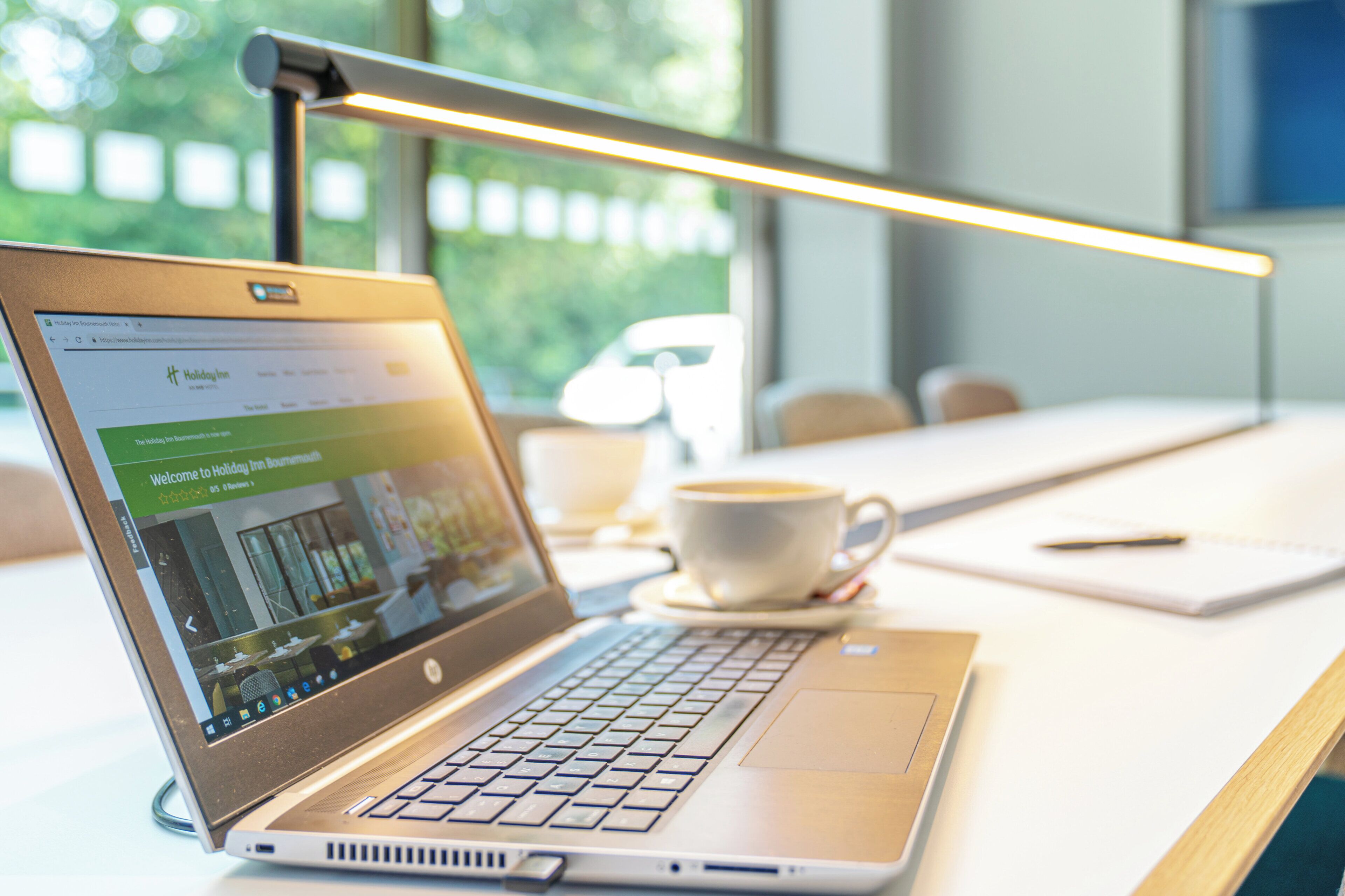 A laptop on a desk with a coffee cup, a pen, and a tablet.