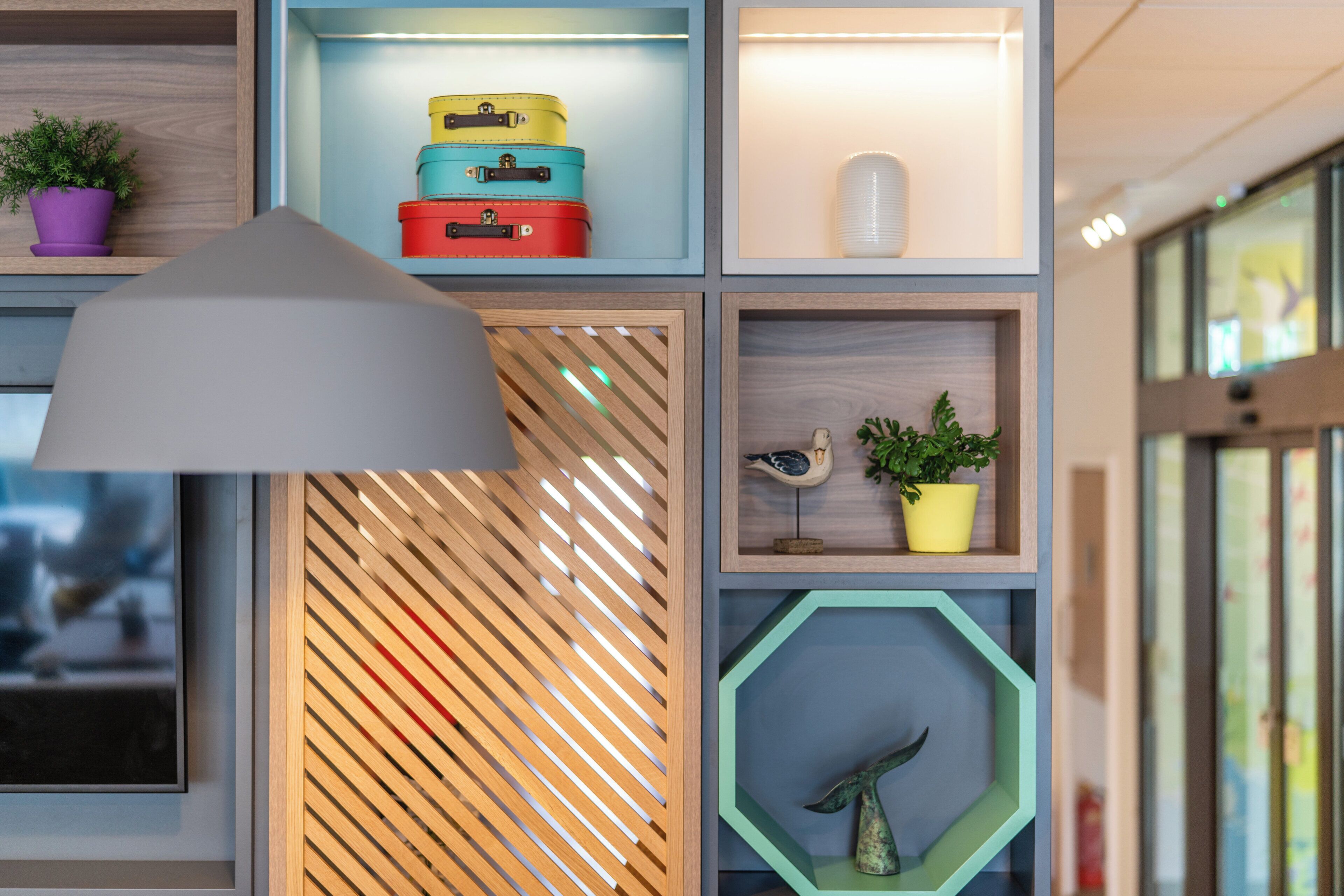 Een muur met meerdere planken waarop diverse voorwerpen staan, zoals een lamp, potplanten en decoratieve objecten.