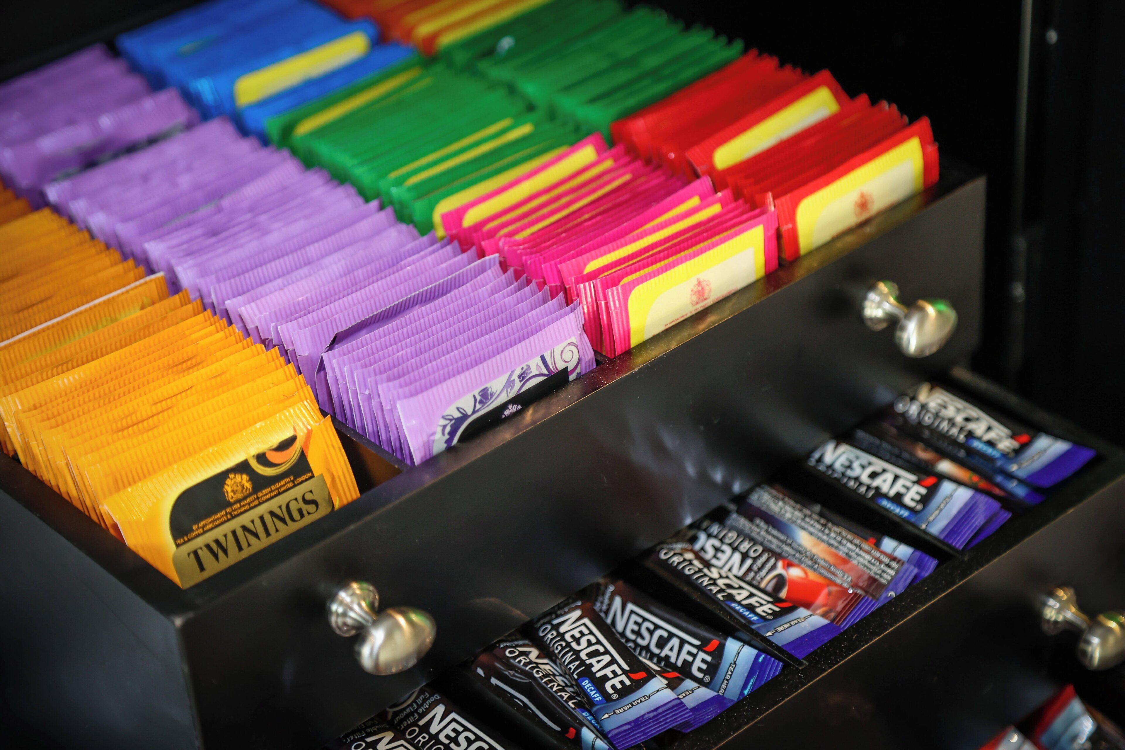 A display of various colored snack packets, including Twinings tea and Nescafe coffee, arranged in a metal rack.