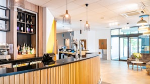 A modern reception area with a wooden reception desk, a wine display, and a seating area with a sofa and a table. - Holiday Inn Bournemouth by IHG (Bournemouth)