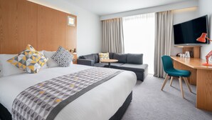 A hotel room with a large bed, a sofa, a desk, a TV, and a window with curtains. - Holiday Inn Bournemouth by IHG (Bournemouth)