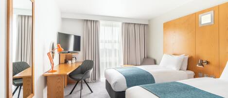 A hotel room with two beds, a desk with a chair, a television, and a large mirror.