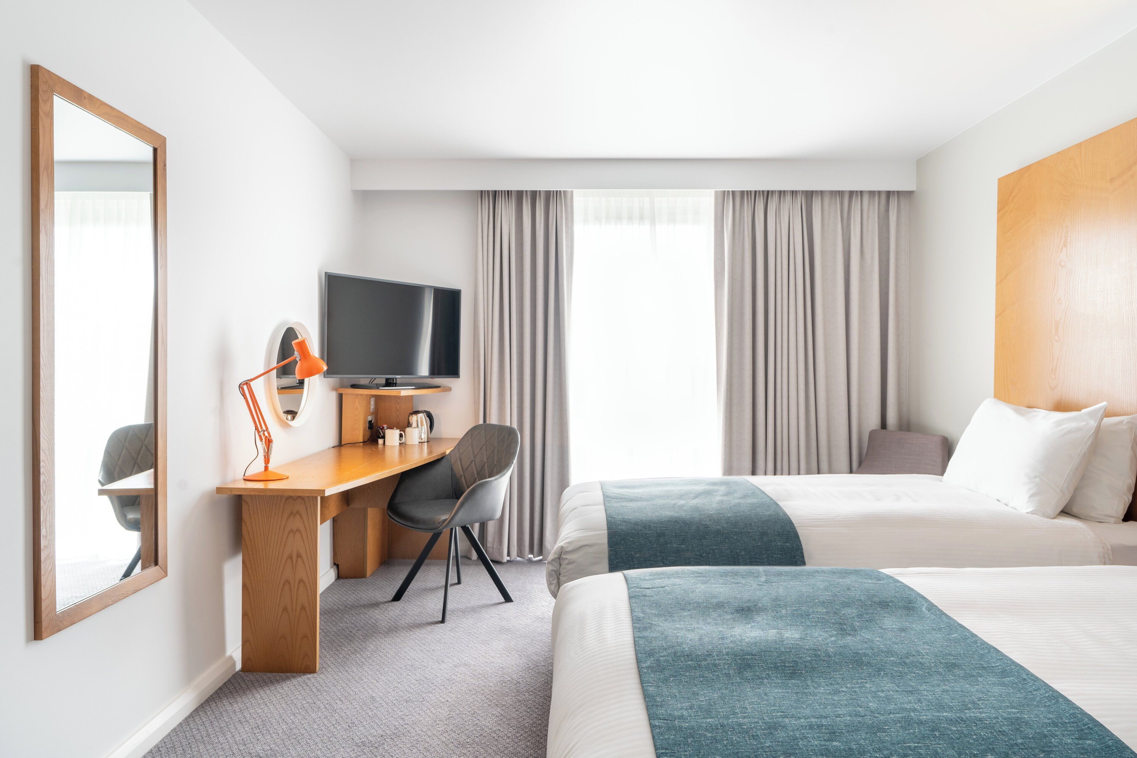 A hotel room with two beds, a desk with a chair, a television, and a large mirror.