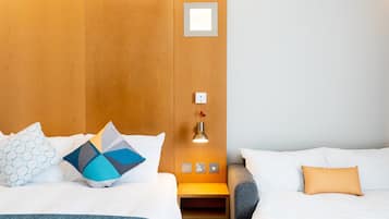Habitación de hotel con dos camas, cabecera de madera, mesita de noche con lámpara y una pequeña estantería.