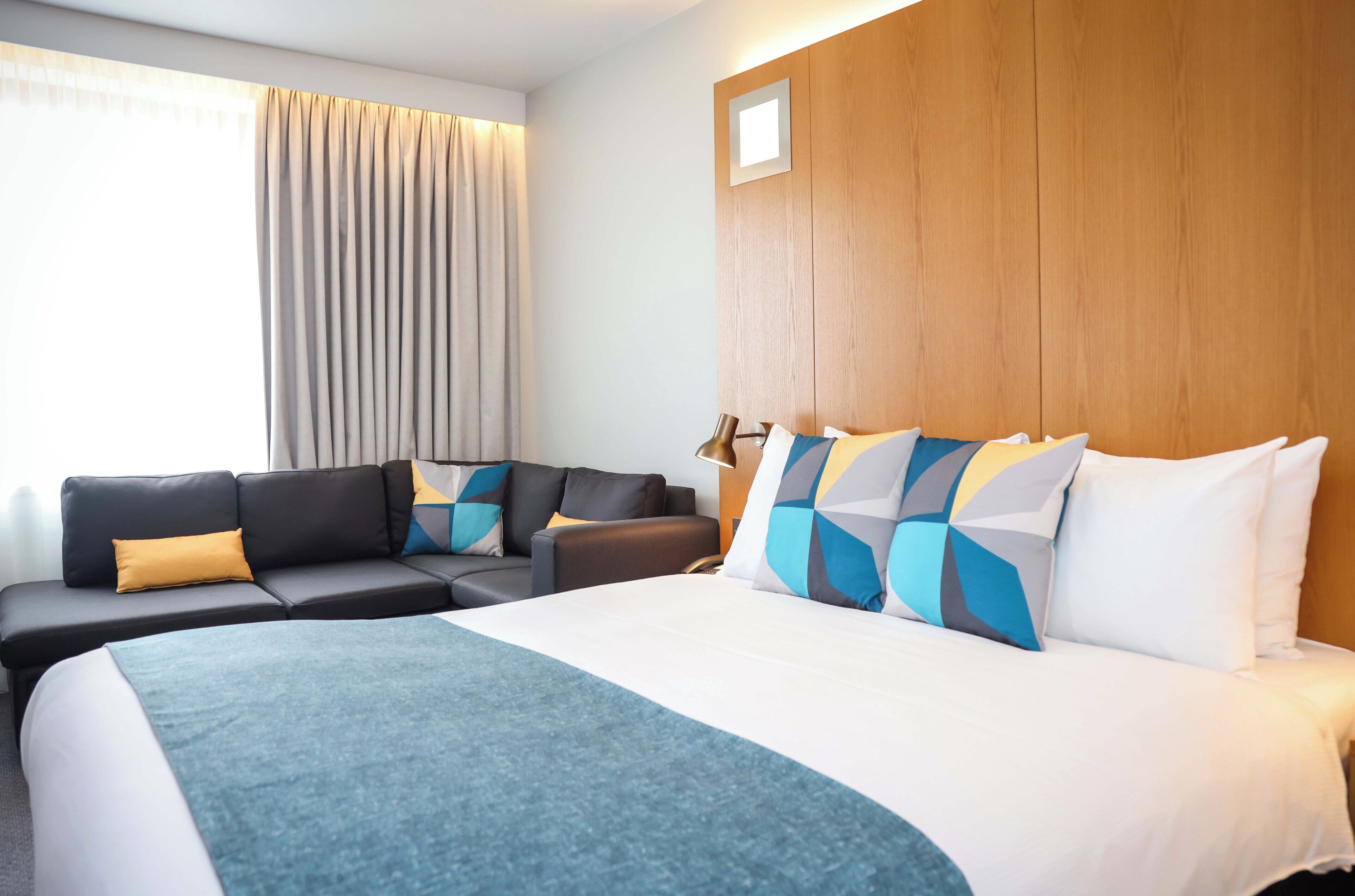 A hotel room with a bed, a sofa, a desk, and a window with curtains.