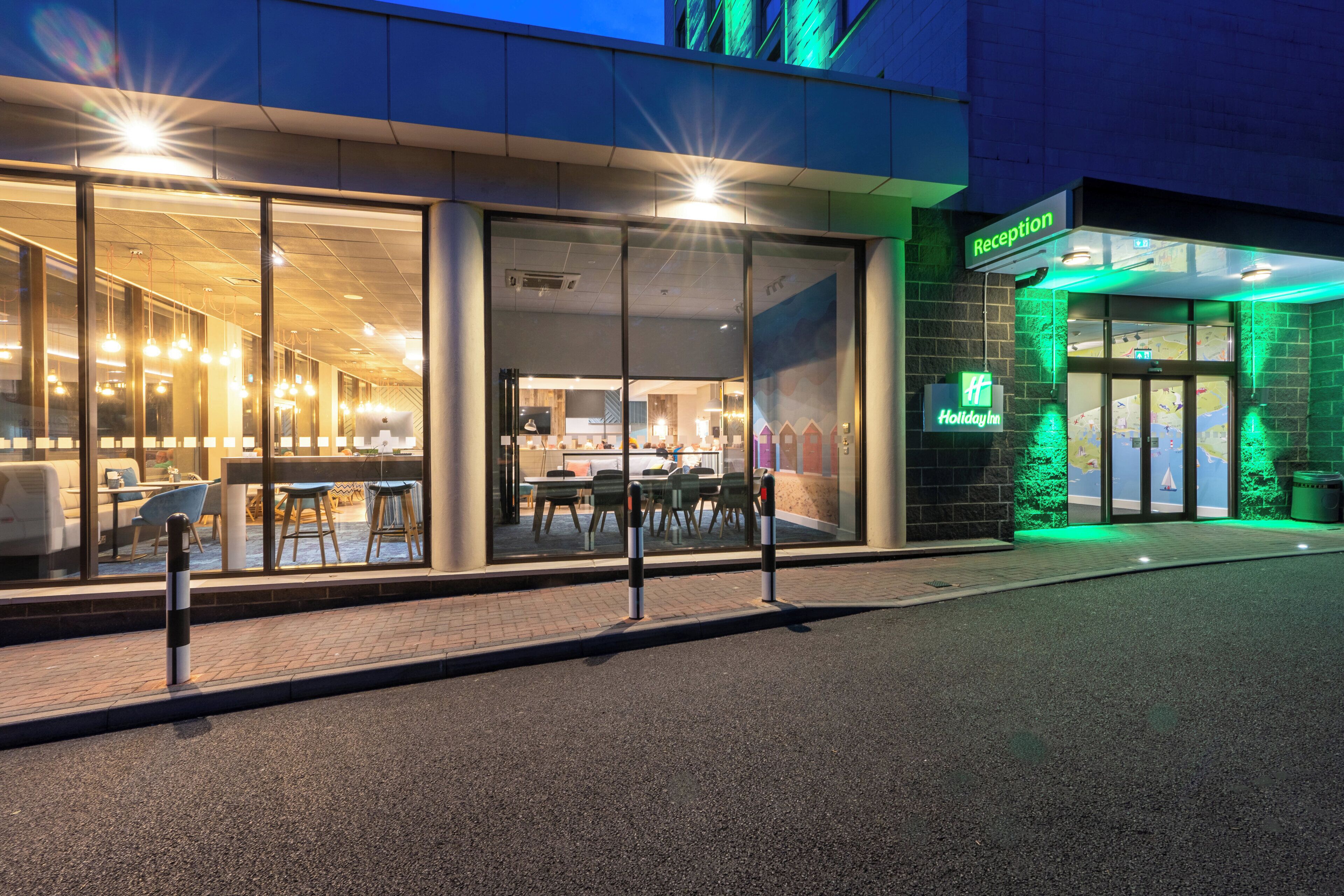 A hotel entrance with a reception desk, a glass facade, and a green-lit exterior.
