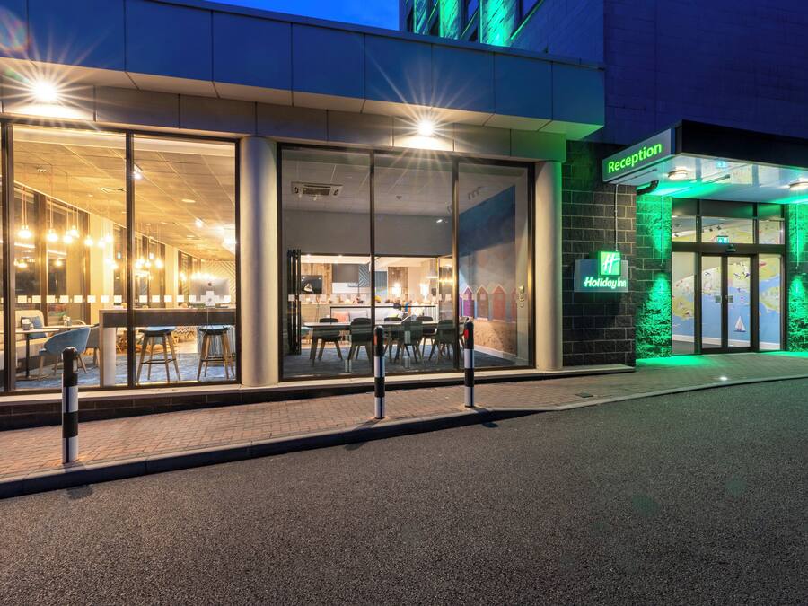 A hotel entrance with a reception desk, a glass facade, and a green-lit exterior.