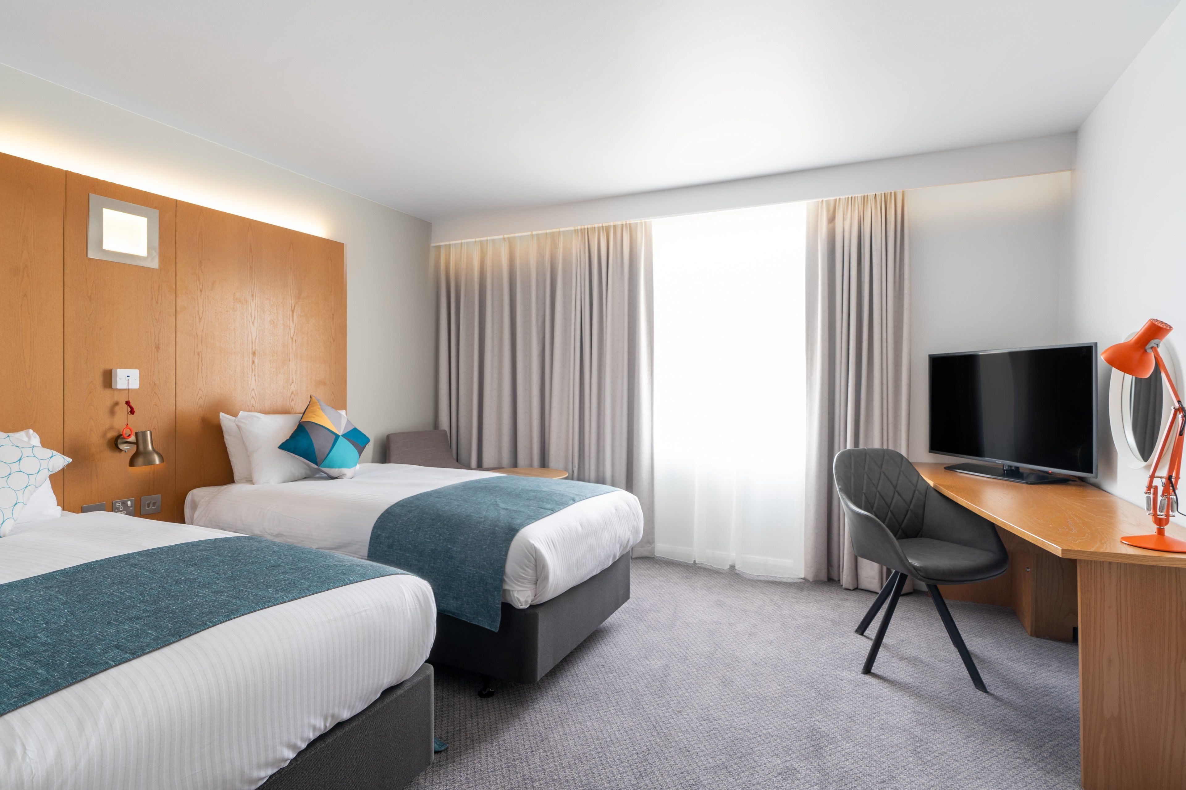 A hotel room with two beds, a desk with a TV, and a chair.