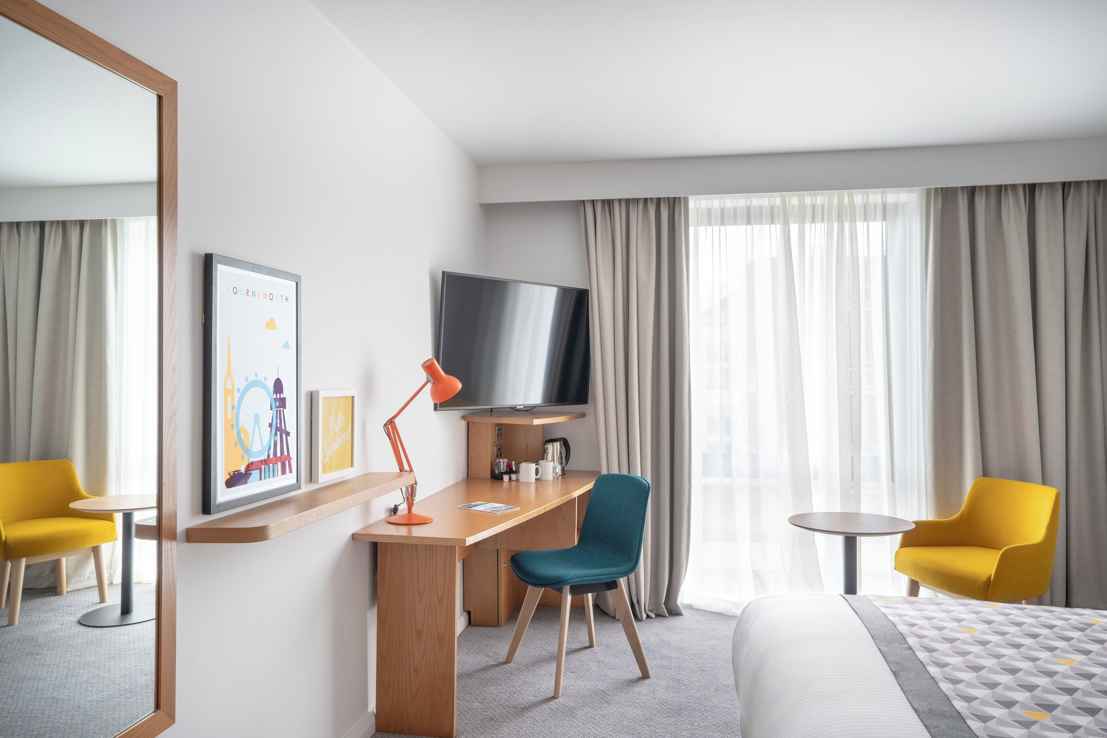 Une chambre d’hôtel comprenant un lit, un bureau avec une chaise, une télévision et un grand miroir.