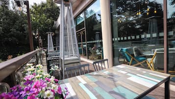 Un área de estar al aire libre con una estructura de metal para parrilla, mesas y sillas de madera.