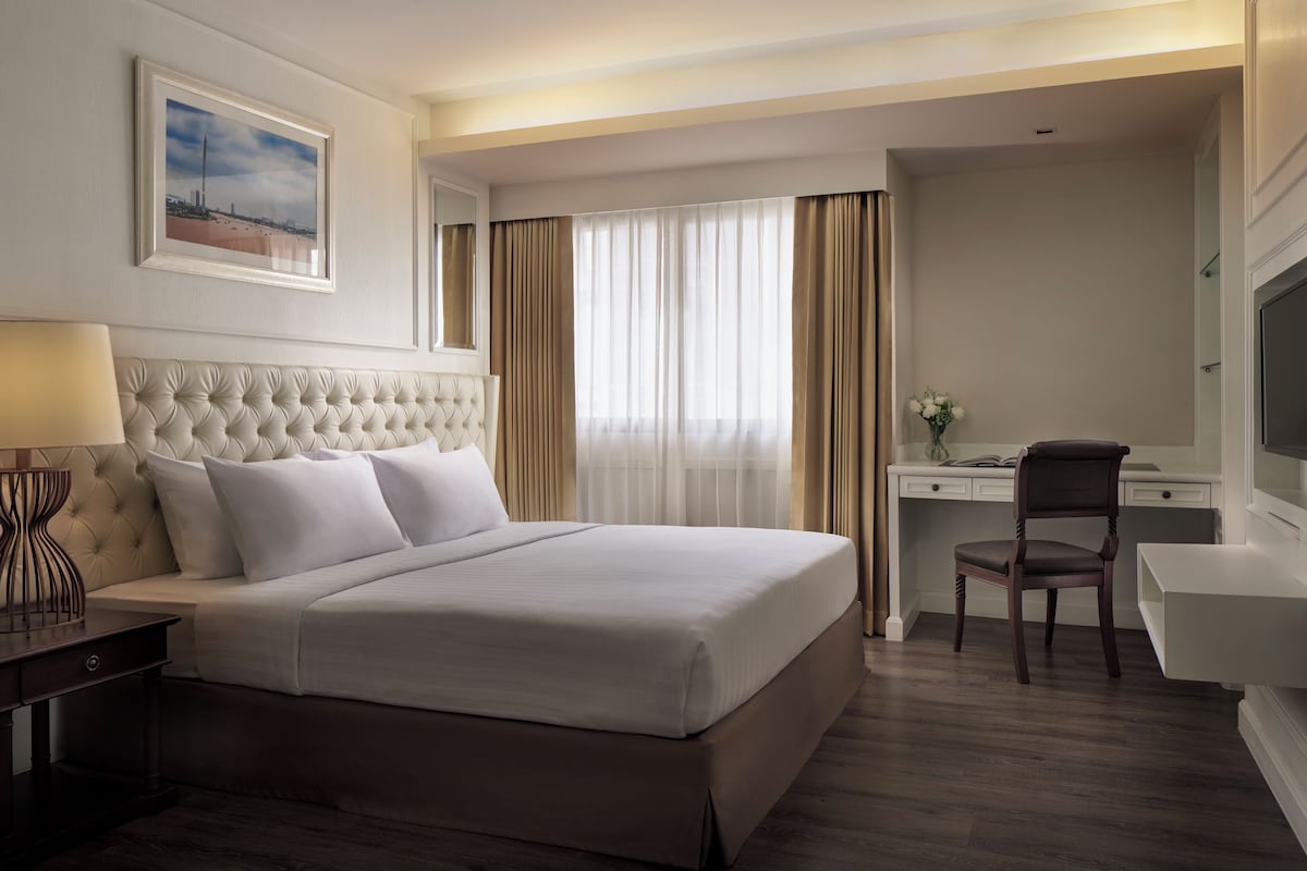 A hotel room with a large bed, a desk, a chair, and a TV.