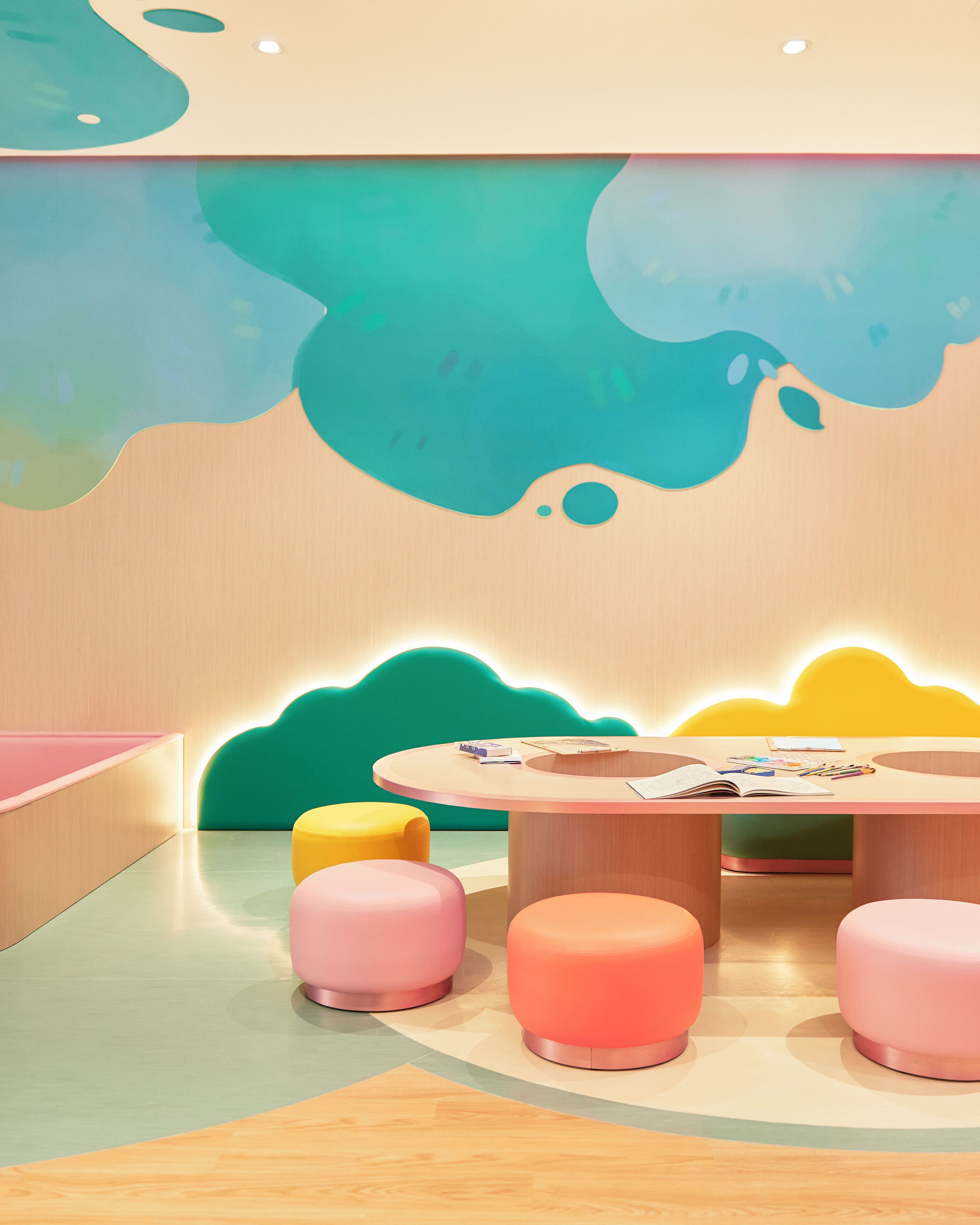 A modern children's play area with a round table, colorful stools, and a vibrant wall mural.