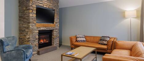 Una sala de estar con chimenea de piedra, un televisor de pantalla plana, un sillón azul, un sofá de cuero naranja y una mesa de centro.