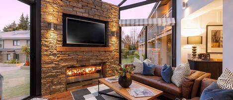 A modern living room with a stone fireplace, leather sofa, and a large TV.
