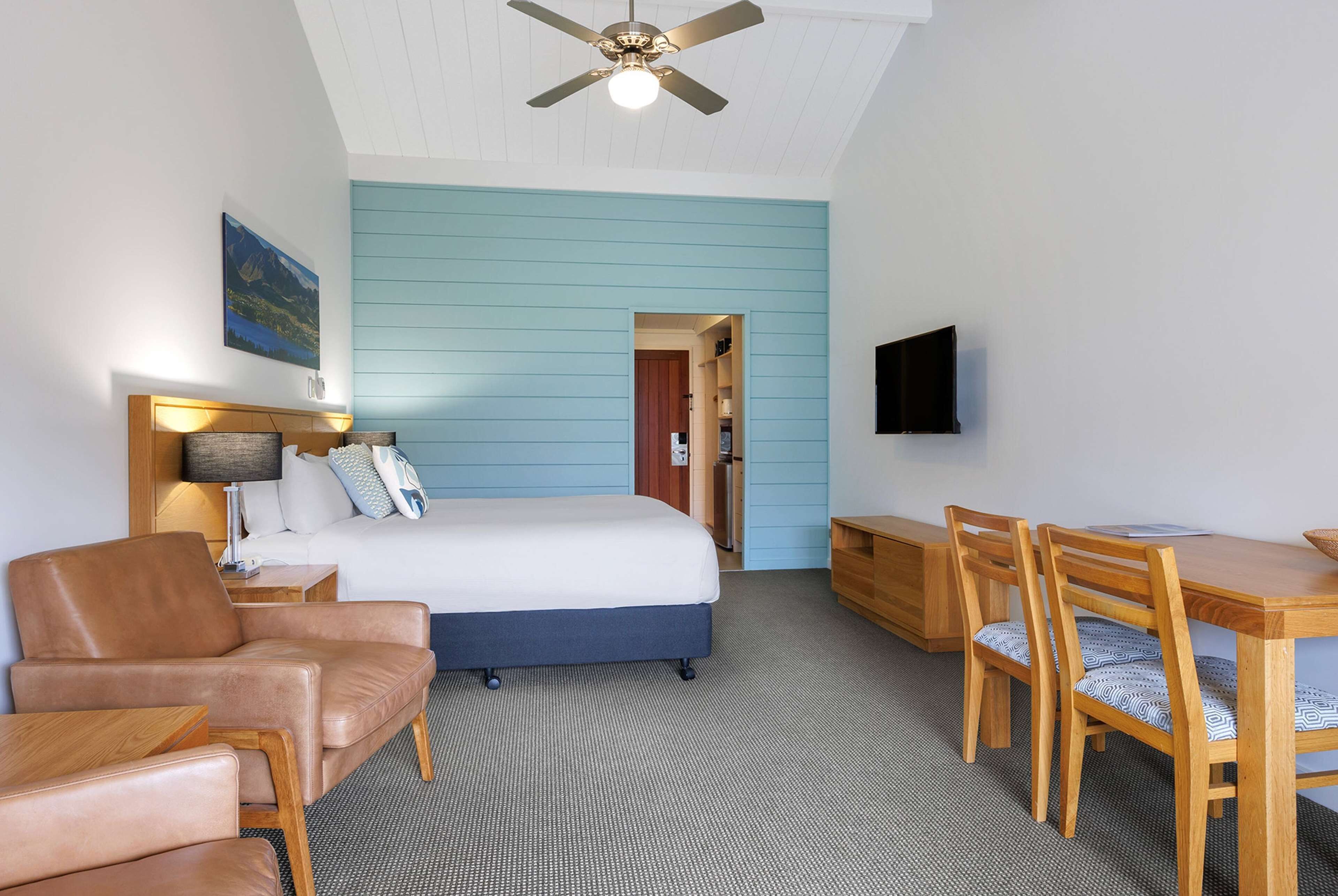 Une chambre d’hôtel équipée d’un lit, d’un bureau, d’une chaise, d’un canapé, d’un ventilateur de plafond et d’un téléviseur fixé au mur.