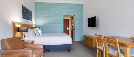 Une chambre d’hôtel équipée d’un lit, d’un bureau, d’une chaise, d’un canapé, d’un ventilateur de plafond et d’un téléviseur fixé au mur.