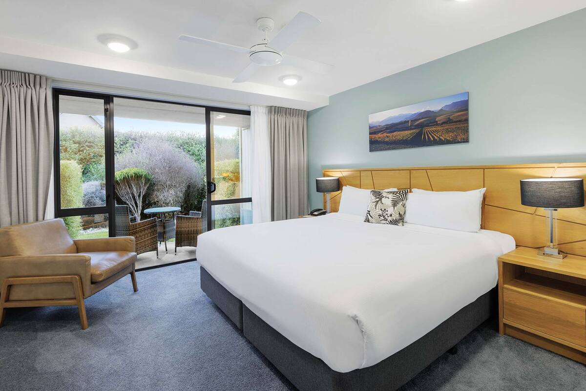 A hotel room with a large bed, a sofa, a small table, and a view of the outdoors.
