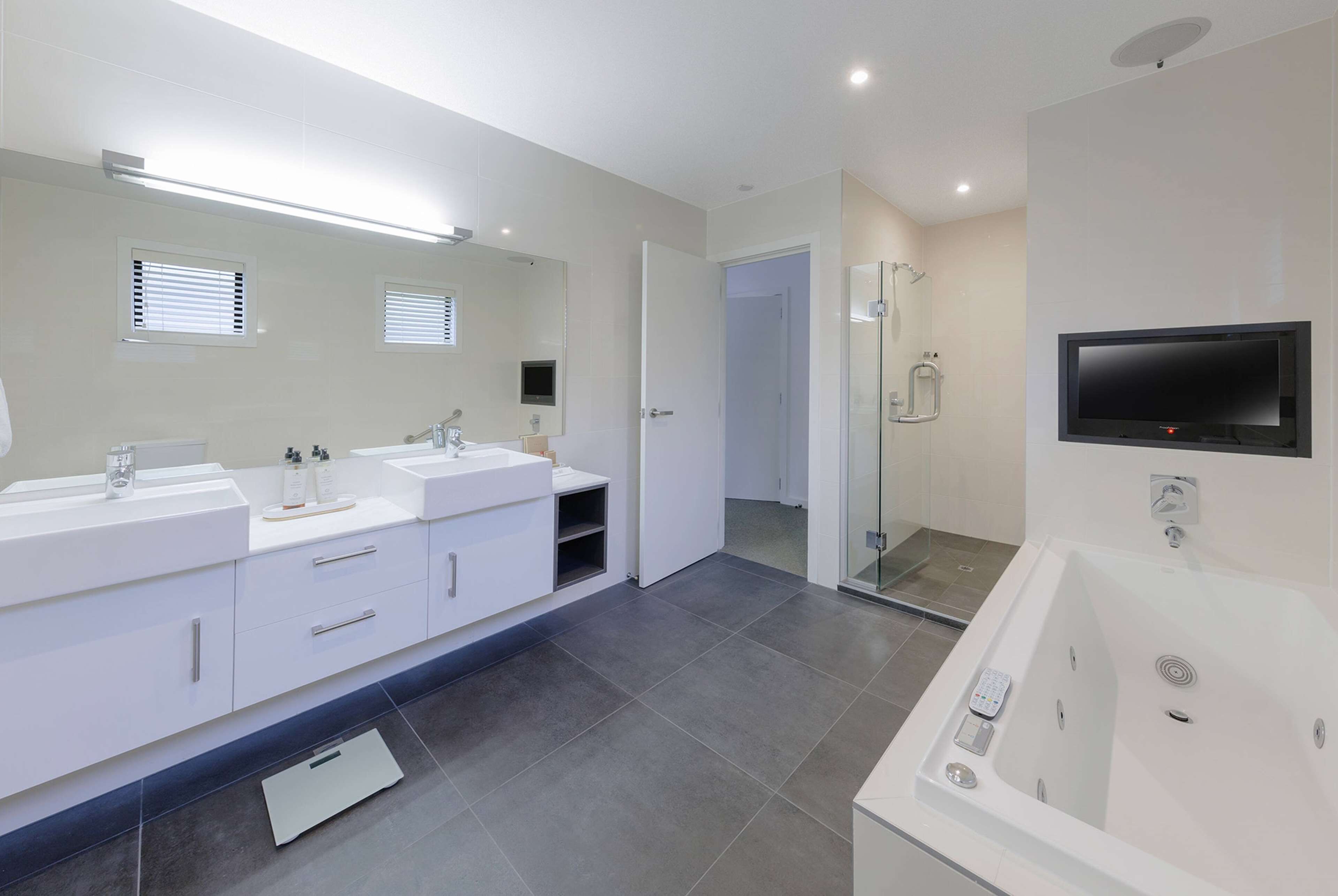 A modern bathroom with two sinks, a large mirror, a shower area, and a built-in TV.