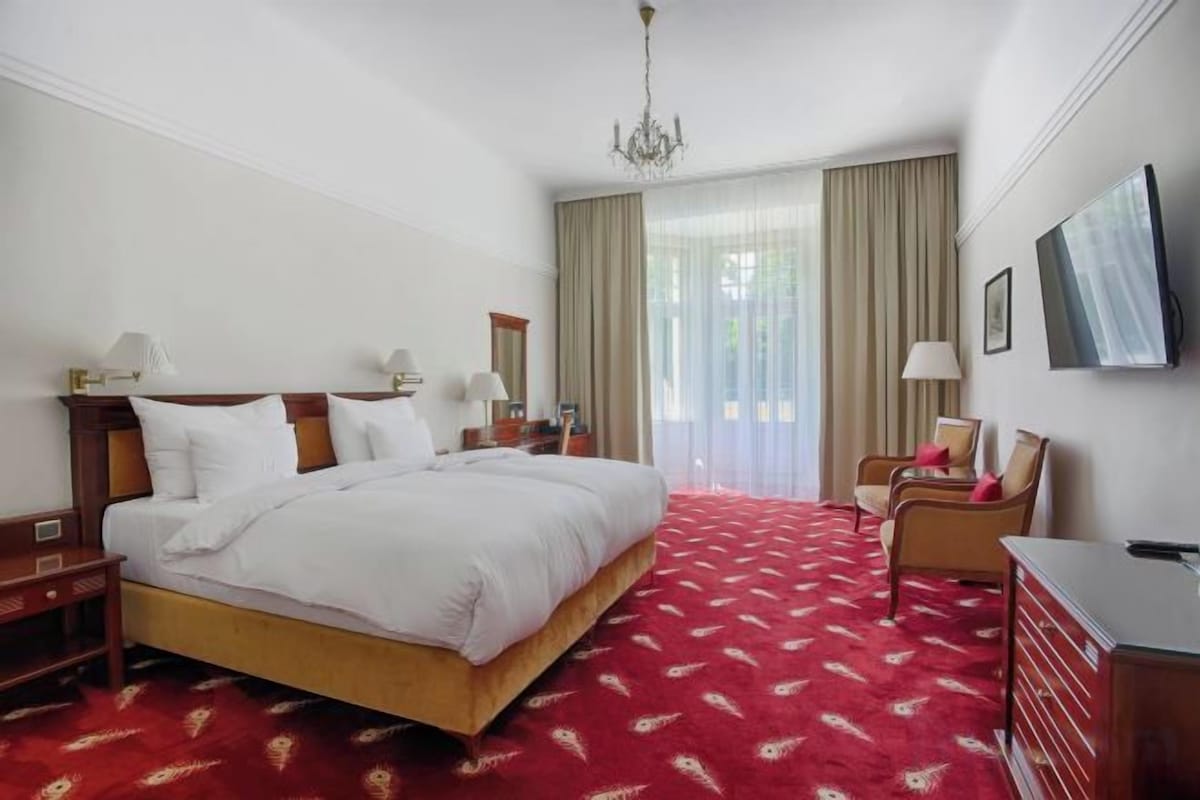 A hotel room with a large bed, bedside tables, a desk, a chair, and a television.