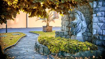 A stone pathway leading to a statue of a figure holding a book, surrounded by greenery and a stone wall.