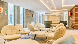 A modern lobby with seating areas, a reception desk, and a glass wall with a view. - Ensana Thermia Palace (Piestany)