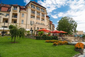 A multi-story hotel with balconies, a garden with orange flowers, and red umbrellas.