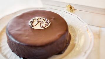 A chocolate cake on a white plate with a logo, placed on a table with a white tablecloth.