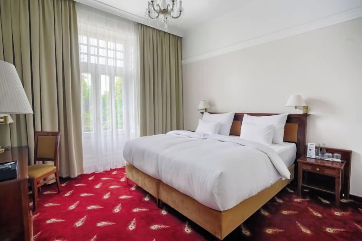 A hotel room with a large bed, a desk, a chair, and a window with curtains.