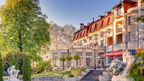 A historic building with a classical facade, a well-maintained garden, and a statue in the foreground. - Ensana Thermia Palace (Piestany)