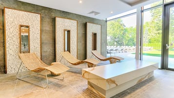 Un espacio interior moderno con un mostrador de recepción de mármol, tres sillones de descanso y ventanas amplias que dan a un jardín ajardinado.