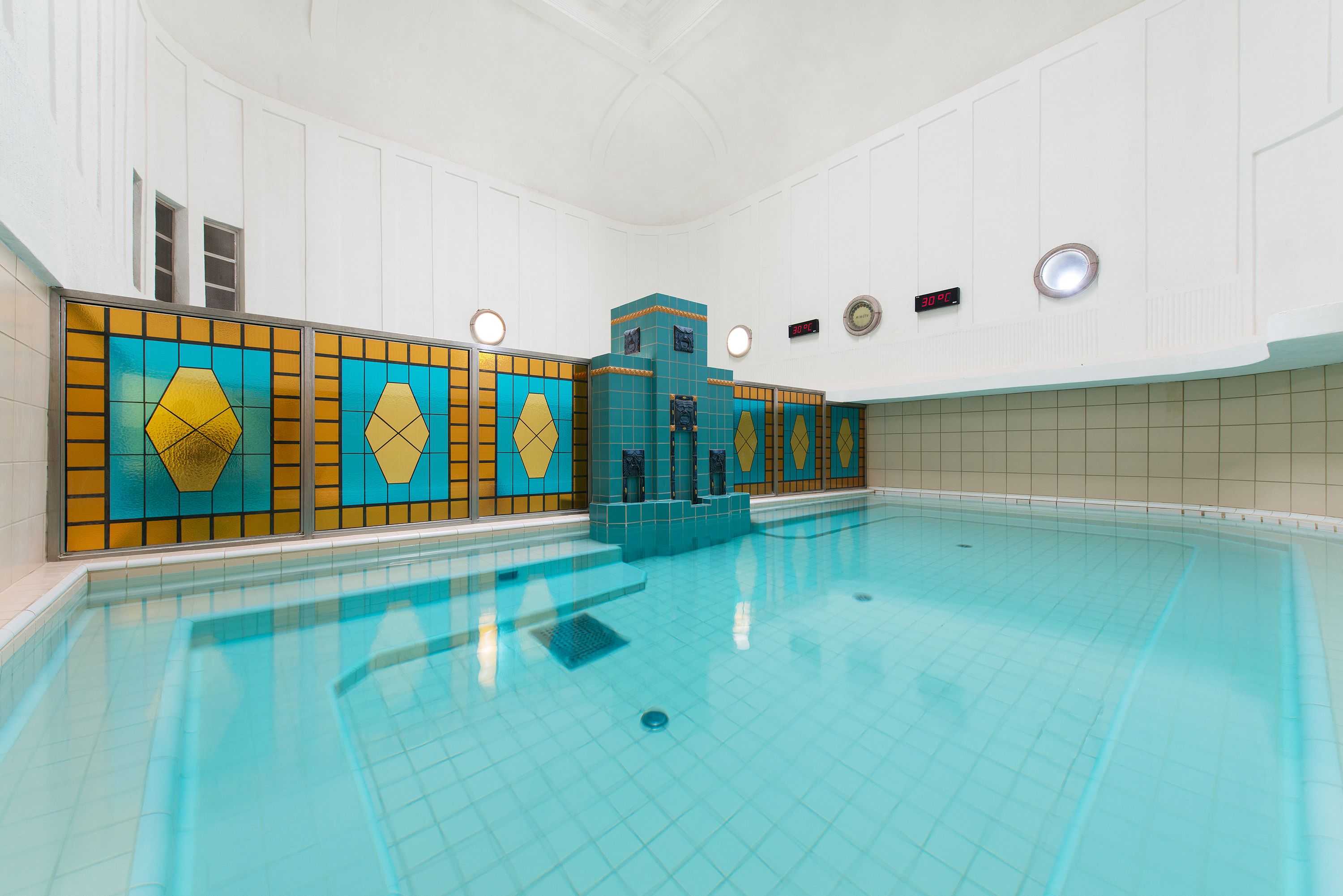 An indoor swimming pool with tiled walls and a clear blue pool.