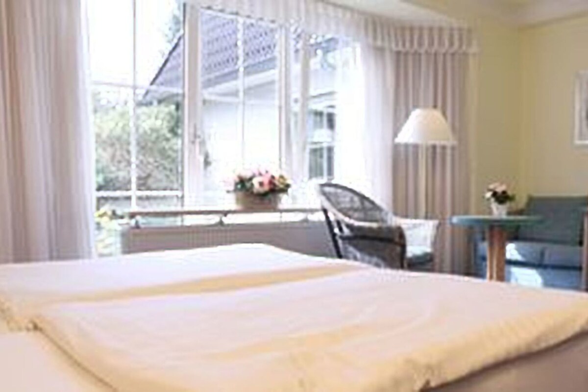 A hotel room with a bed, a desk, a chair, and a window with curtains.