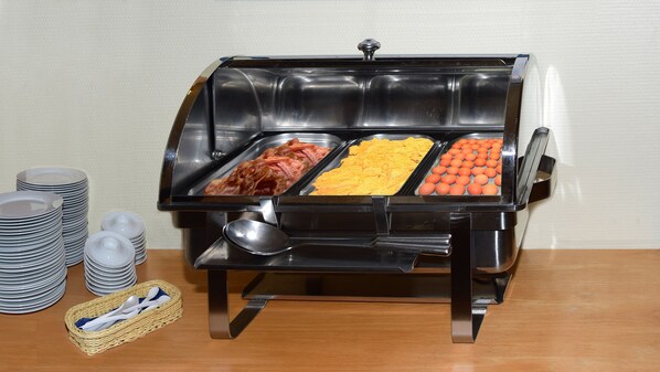 A buffet setup with multiple food trays, including meats, cheese, and eggs.