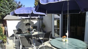 An outdoor patio with a glass table and chairs, covered by a blue umbrella. - Hotel Nordic (Norderstedt)